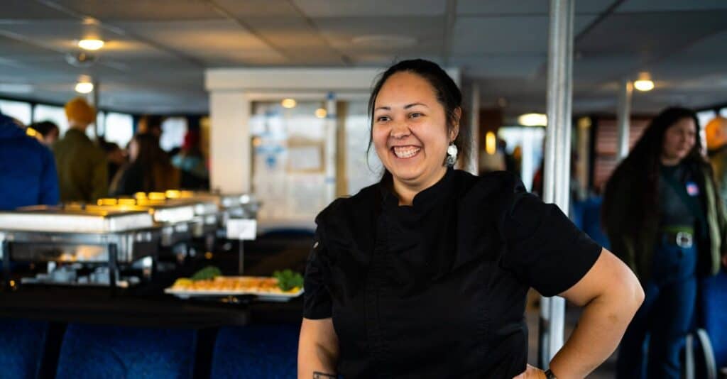 A woman in black smiles. Catering trays can be seen in the background.