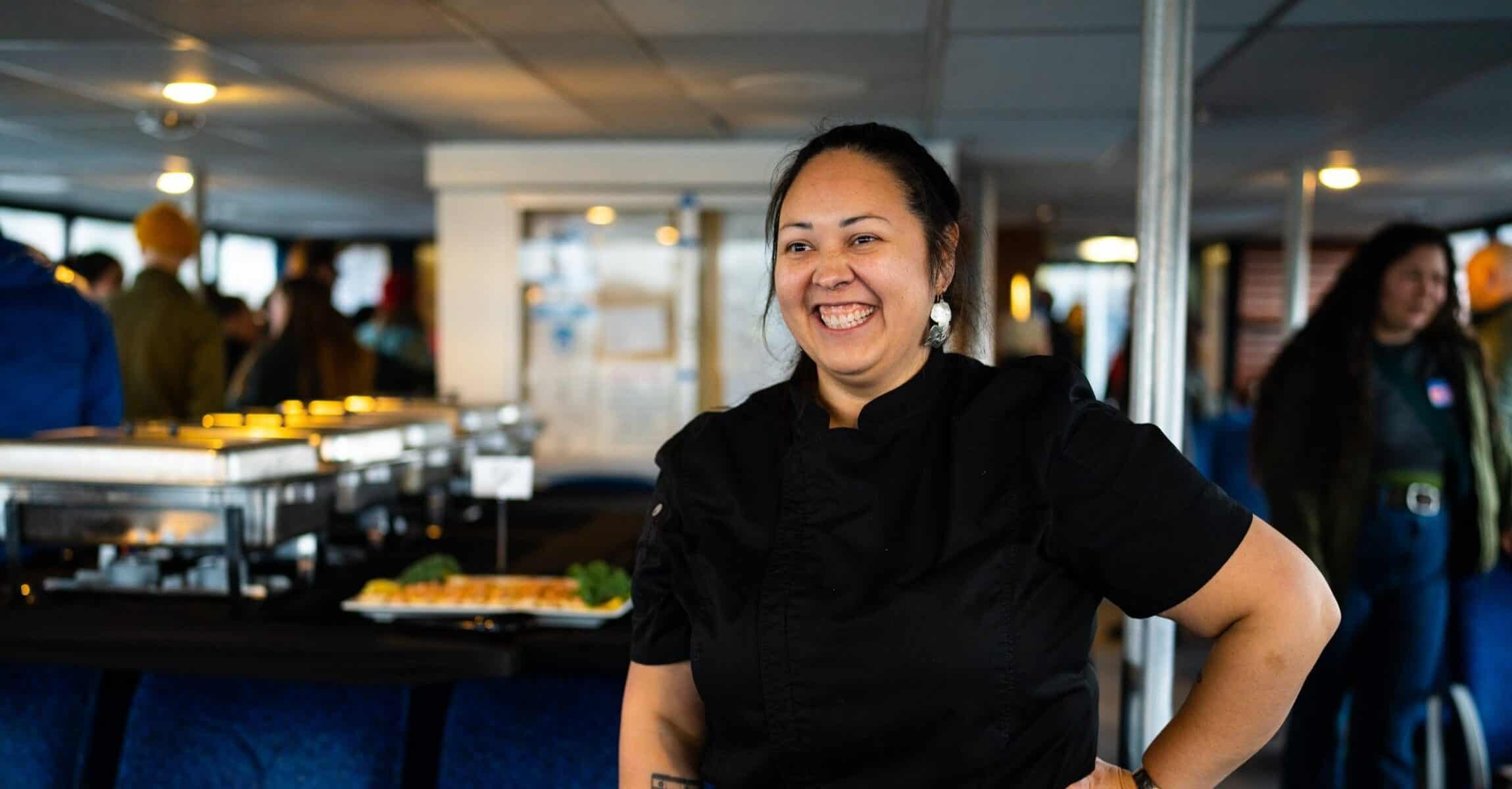 A woman in black smiles. Catering trays can be seen in the background.
