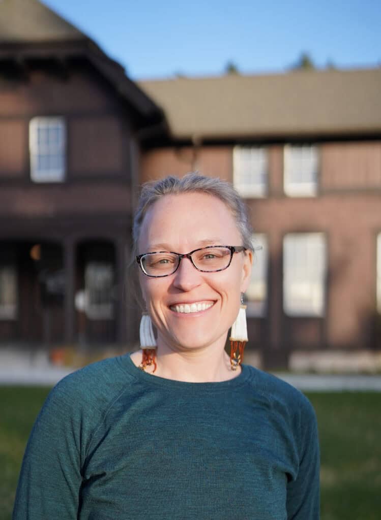 A woman in green and beaded earrings smiling.