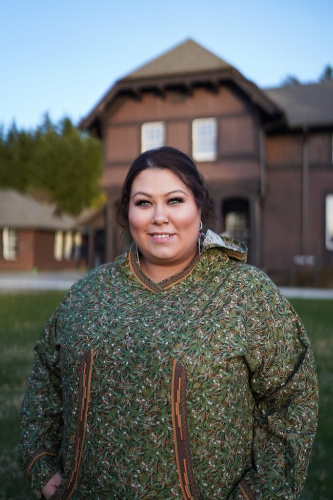 A woman in a green kuspuk stands in front of a building.