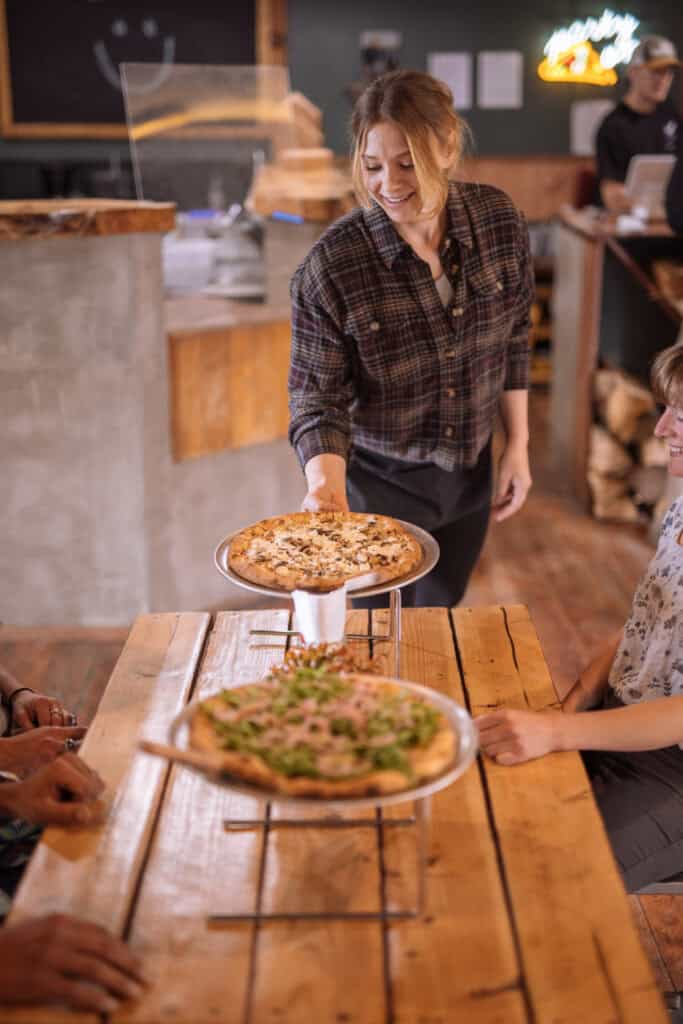A smiling woman delivers pizza in Haines, AK's Alpenglow