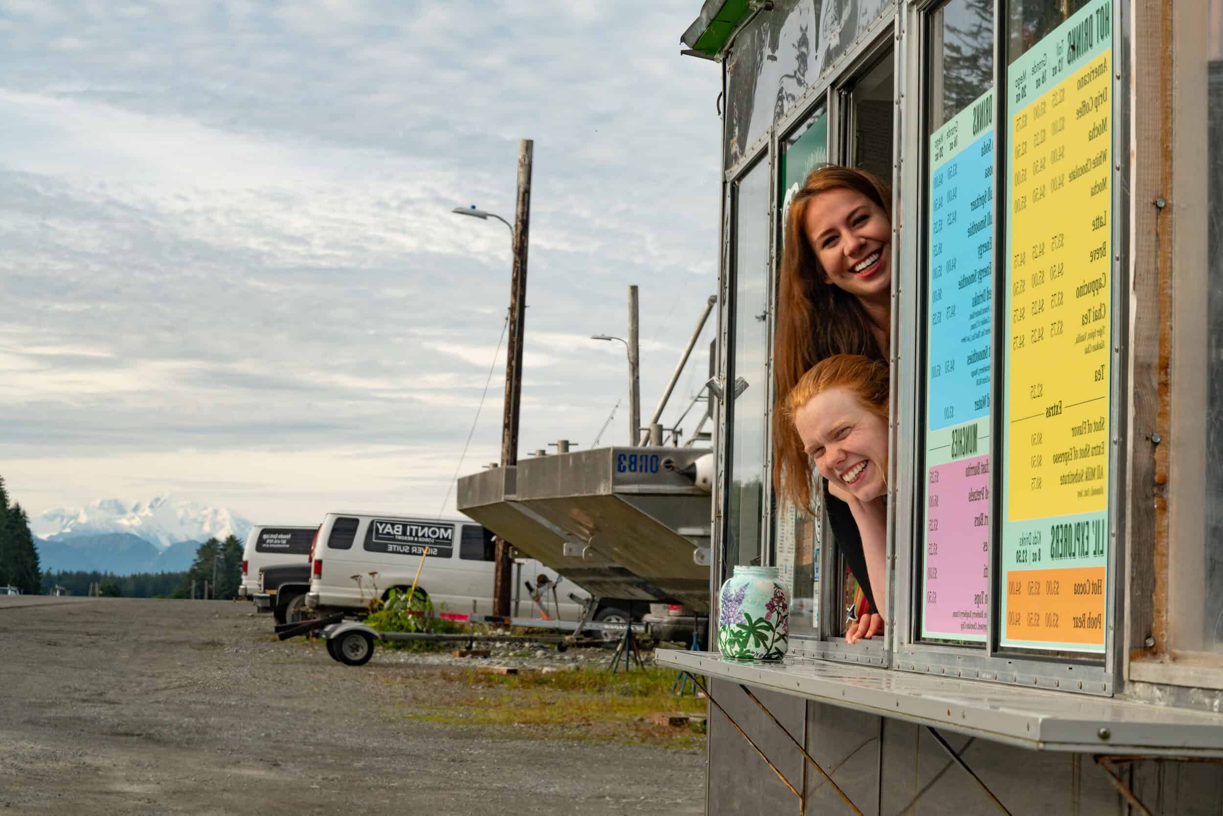 Two people smile brightly as they stick their heads out the window of Village Coffee Co in Yakutat.