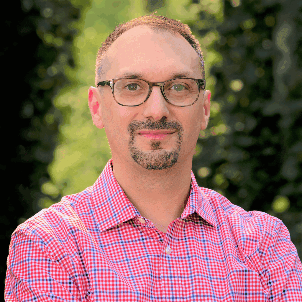A headshot of Chris Perez against a wooded background.
