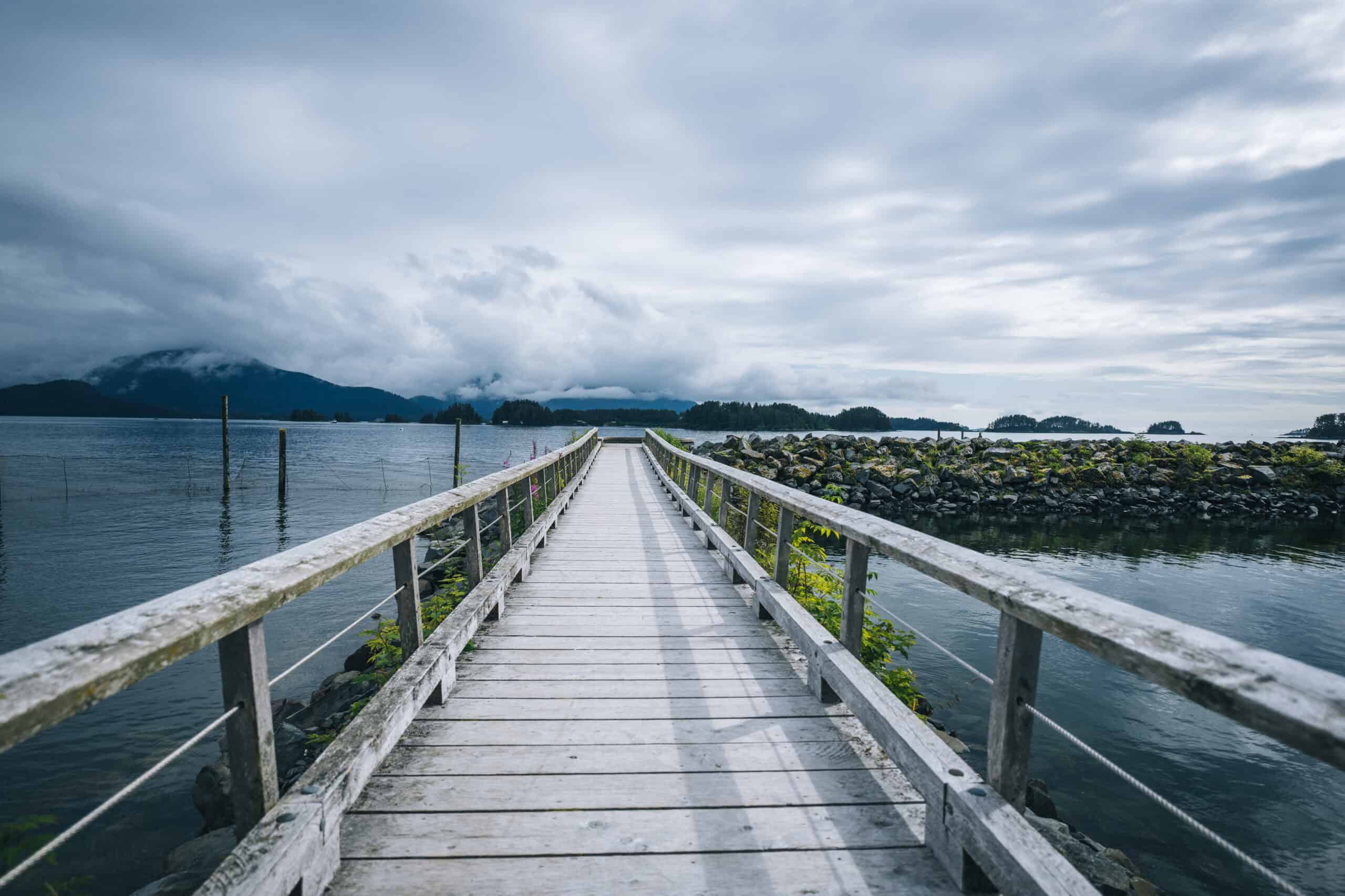 A boardwalk going out into the sea, with mountains in the background.