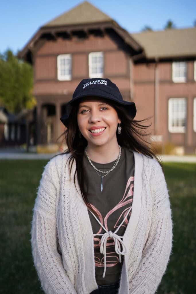 A woman wearing a hat and a sweater in front of a house.