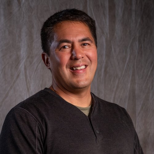 A man in a black shirt smiling for the camera.