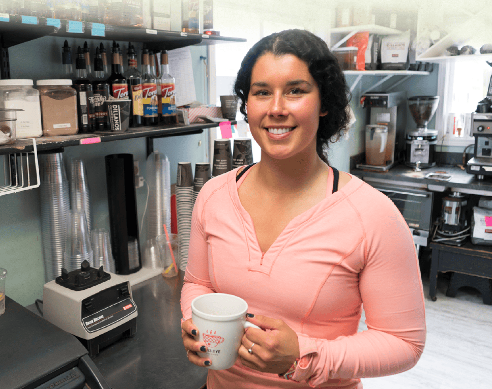 Caitlin Way holding a cup of coffee in her business, Fisheye Coffee.