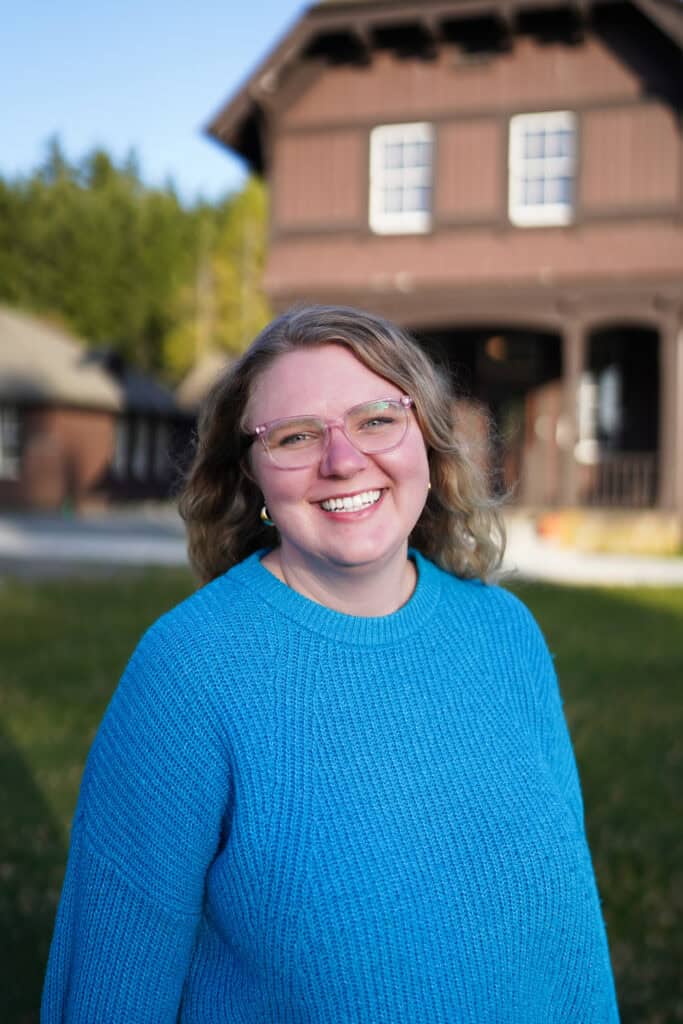 A woman in a blue sweater and glasses standing in front of a house.