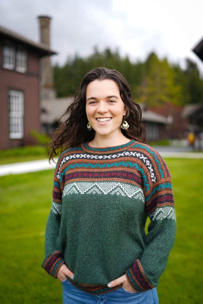 A woman in a green sweater stands in front of a house.