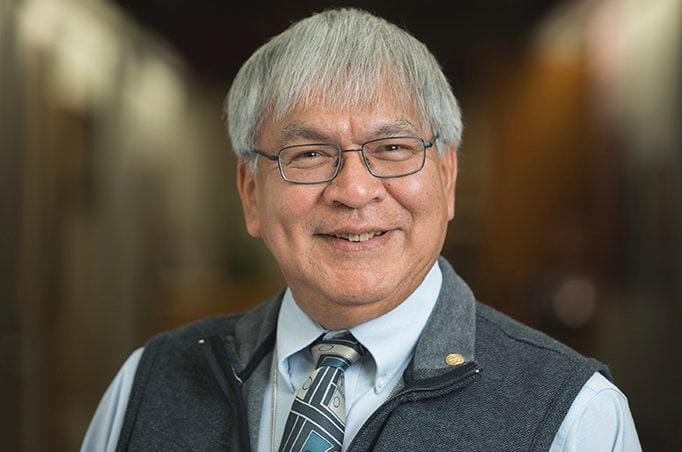 A man with glasses and a vest smiling.
