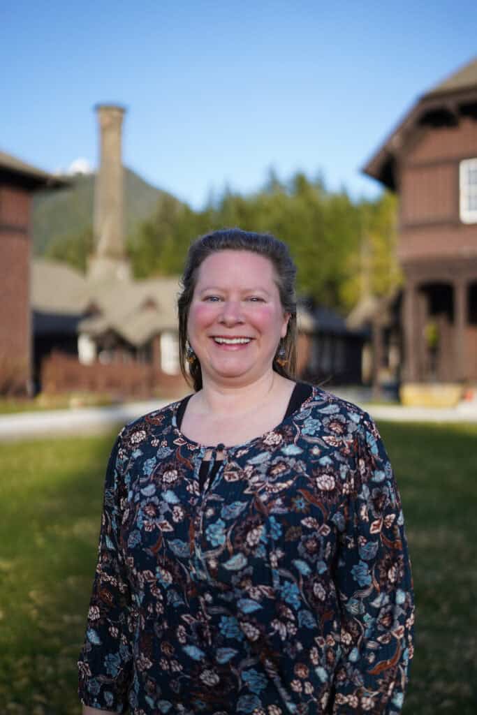 A woman in a floral shirt stands in front of a building.