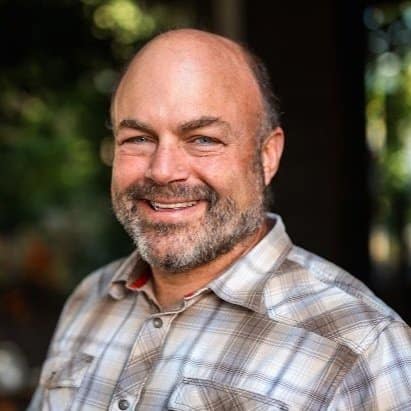 A man with a beard and plaid shirt smiling.