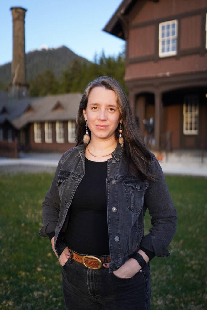 A woman in a black shirt and denim jacket standing in front of a building.