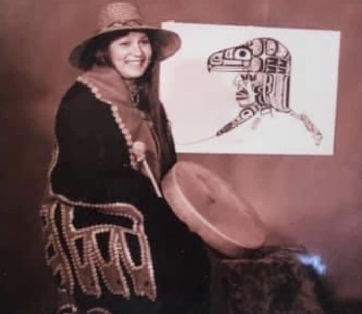 A woman in regalia holding a drum.