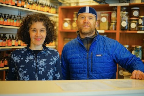 A man and woman standing in front of a shelf of bottles.