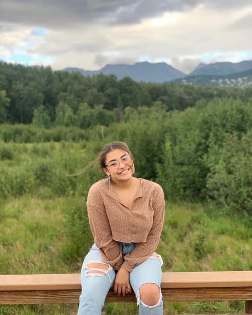 A girl sitting on a bench in front of a field.