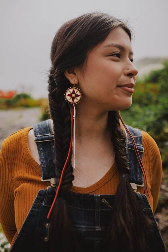 A woman with long braids wearing a yellow top and red earrings.