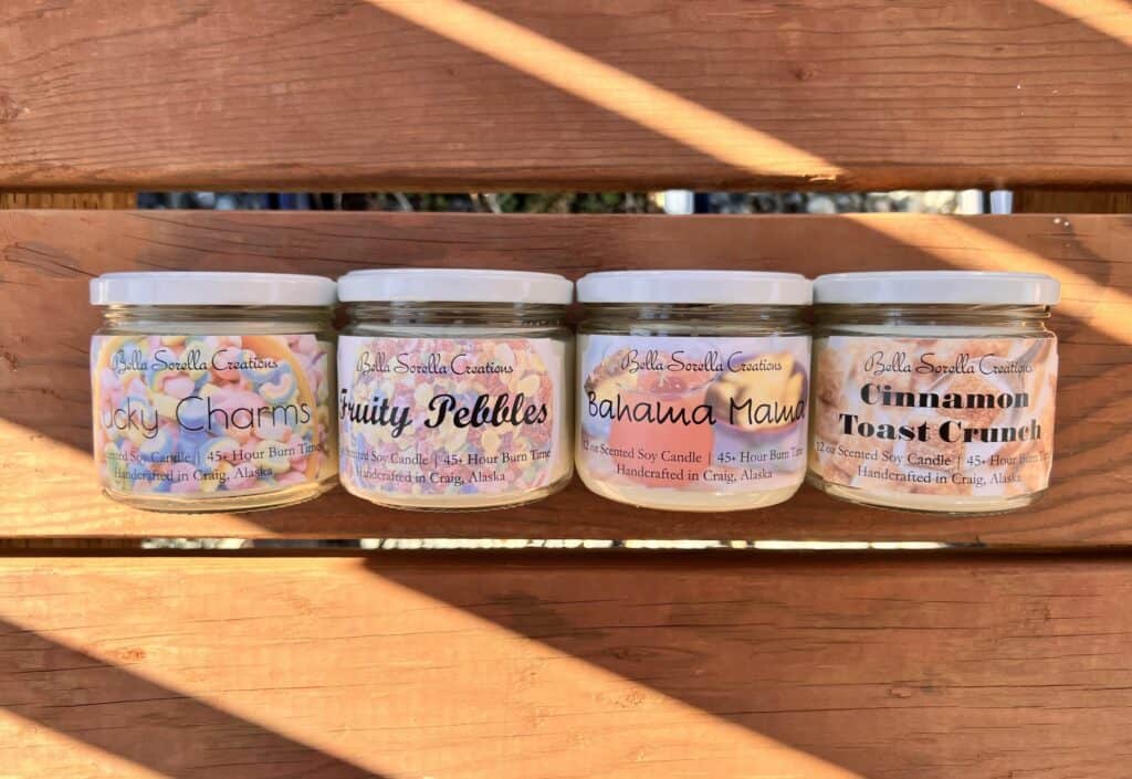 Four jars of different scented candles on a wooden bench.