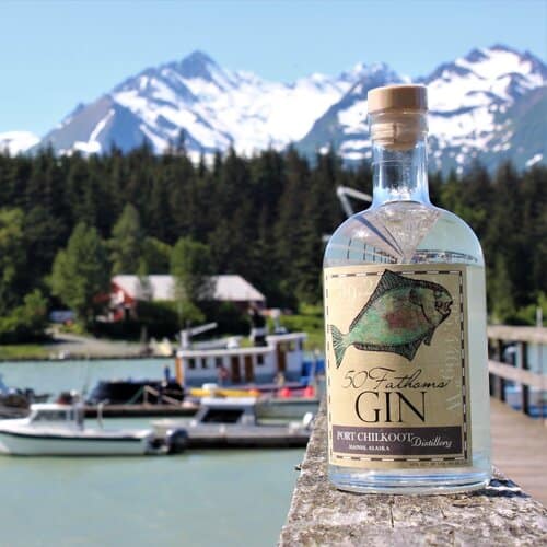 A bottle of gin sitting on a wooden board with mountains in the background.