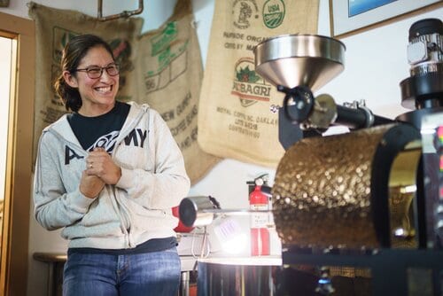 A woman smiling while standing in front of a coffee machine.