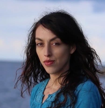 A woman with long hair standing near the ocean.